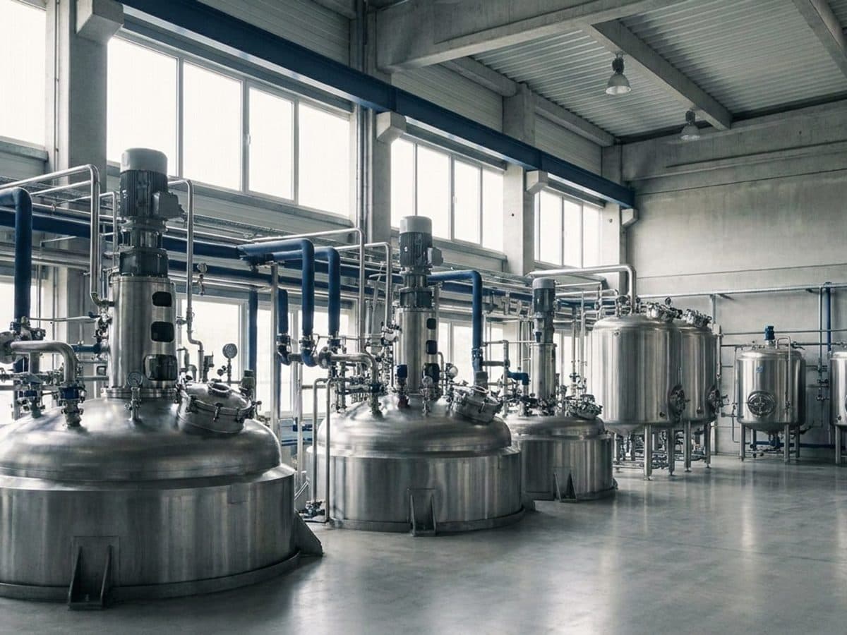 Stainless steel processing vessels and pipes in an industrial hall.
